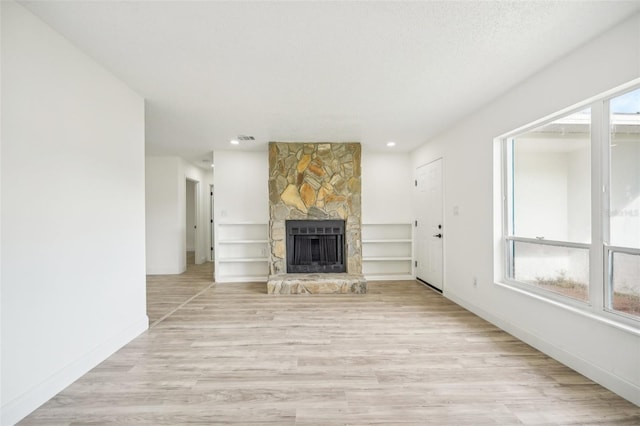 unfurnished living room featuring a textured ceiling, a stone fireplace, and light hardwood / wood-style floors