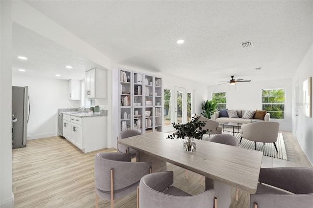 dining space featuring light wood-type flooring, ceiling fan, sink, and a textured ceiling