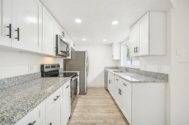 kitchen featuring appliances with stainless steel finishes, light stone countertops, white cabinetry, and light hardwood / wood-style flooring