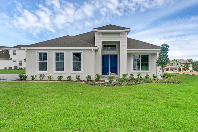 prairie-style home with a front yard, stucco siding, and a shingled roof