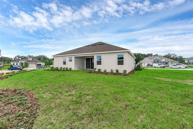 back of property with stucco siding, a shingled roof, and a yard