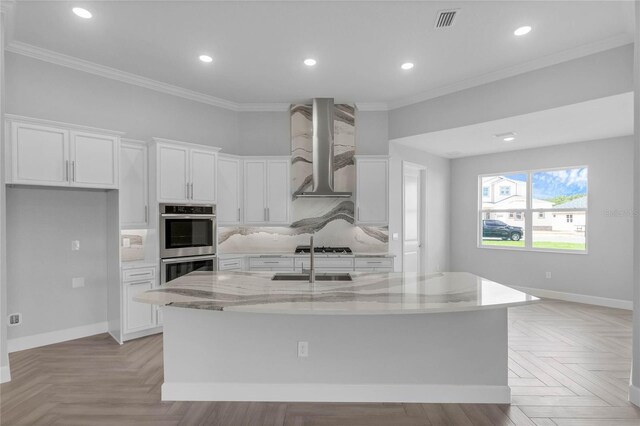 kitchen featuring white cabinetry, stainless steel appliances, a center island with sink, and wall chimney range hood