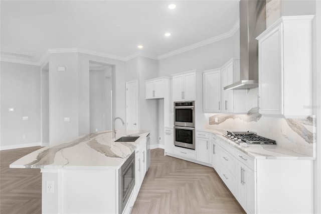 kitchen featuring appliances with stainless steel finishes, white cabinetry, sink, wall chimney range hood, and a center island with sink