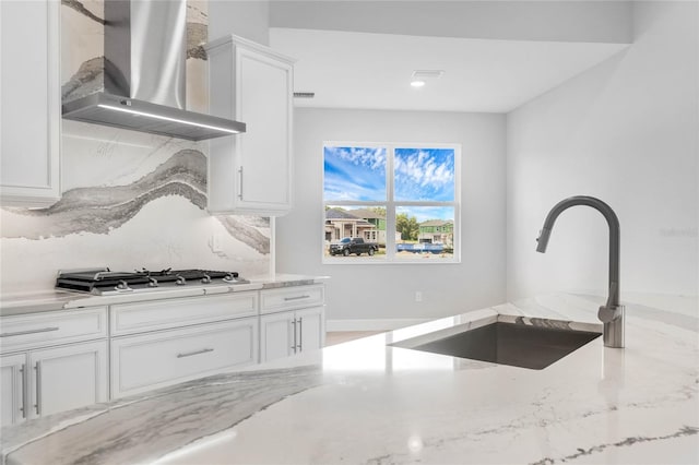 kitchen featuring white cabinetry, stainless steel gas stovetop, light stone counters, sink, and wall chimney range hood