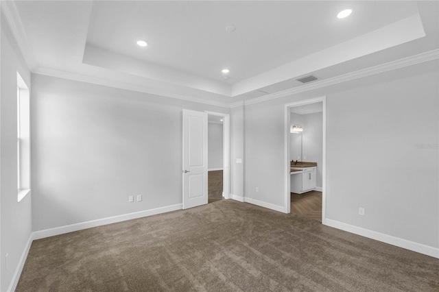 unfurnished bedroom featuring a tray ceiling, dark colored carpet, connected bathroom, and ornamental molding