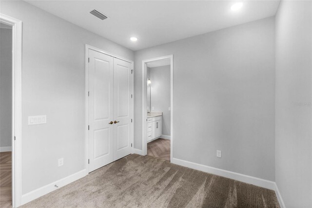 unfurnished bedroom featuring connected bathroom, light colored carpet, and a closet