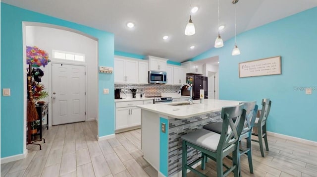 kitchen featuring stainless steel appliances, sink, hanging light fixtures, vaulted ceiling, and white cabinets