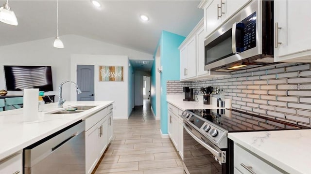 kitchen with vaulted ceiling, appliances with stainless steel finishes, hanging light fixtures, sink, and white cabinets