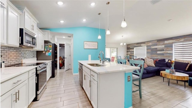 kitchen featuring hanging light fixtures, appliances with stainless steel finishes, sink, lofted ceiling, and a center island with sink