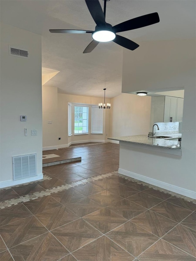 unfurnished living room with dark parquet flooring, ceiling fan with notable chandelier, and sink