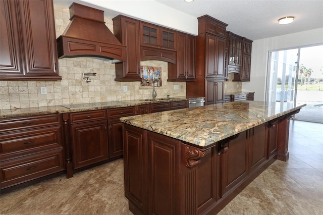 kitchen with light stone countertops, premium range hood, black electric cooktop, sink, and a center island