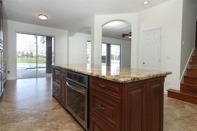 kitchen featuring a center island, stainless steel microwave, ceiling fan, light stone countertops, and a textured ceiling