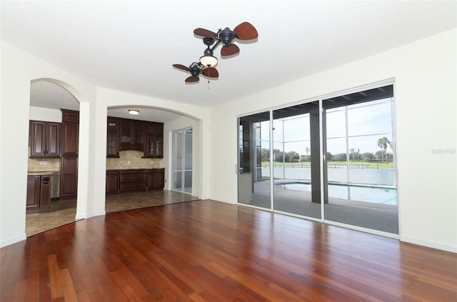 unfurnished living room featuring dark hardwood / wood-style floors, ceiling fan, a water view, and a textured ceiling