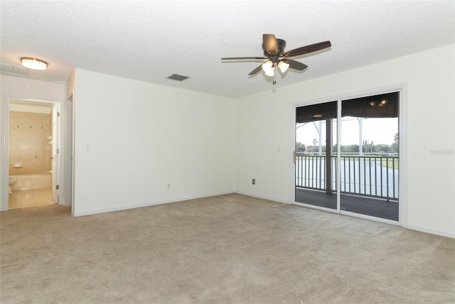 empty room with light carpet, a textured ceiling, a water view, and ceiling fan