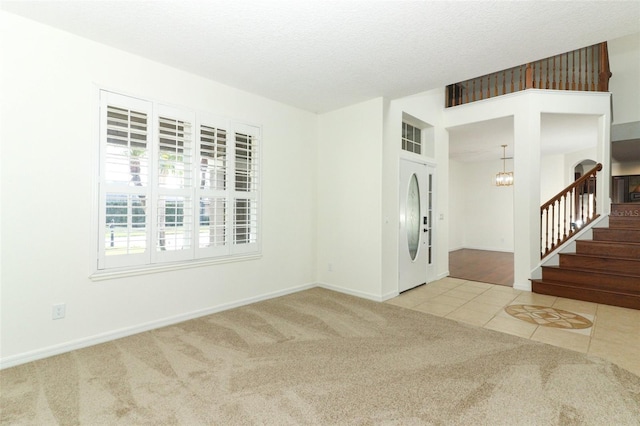 foyer featuring an inviting chandelier, carpet flooring, and a textured ceiling