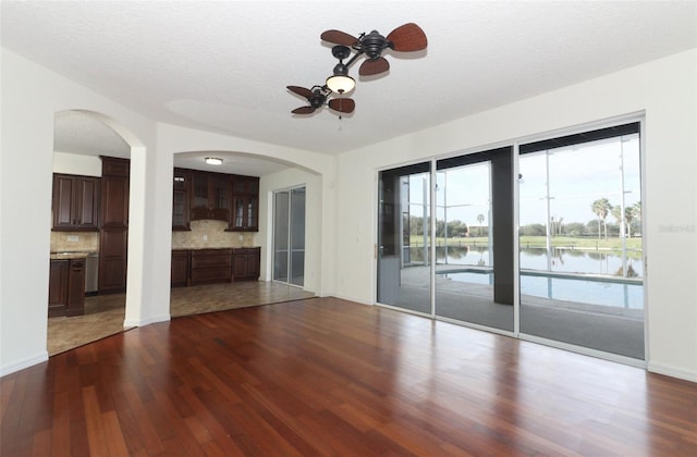 unfurnished living room featuring a water view, ceiling fan, dark wood-type flooring, and a textured ceiling