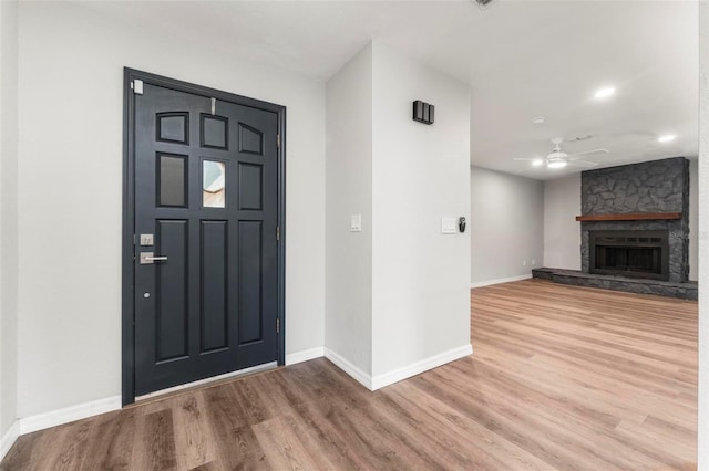 entryway with ceiling fan, a stone fireplace, and wood-type flooring