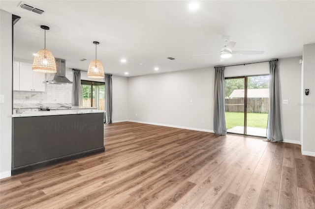 kitchen with light hardwood / wood-style flooring, white cabinets, wall chimney exhaust hood, and a healthy amount of sunlight