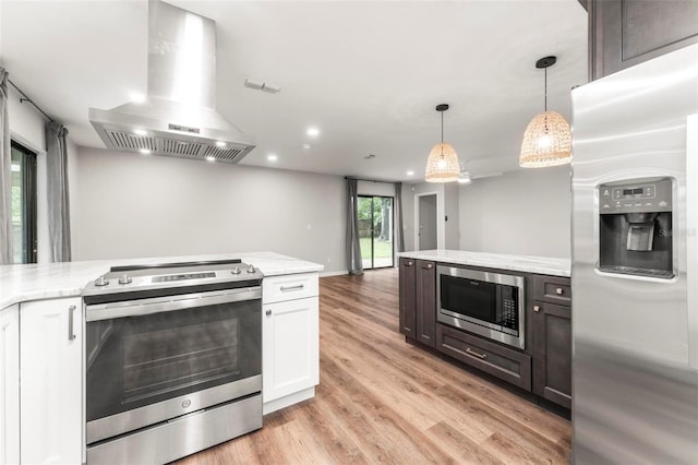 kitchen featuring white cabinets, appliances with stainless steel finishes, light hardwood / wood-style floors, wall chimney range hood, and pendant lighting