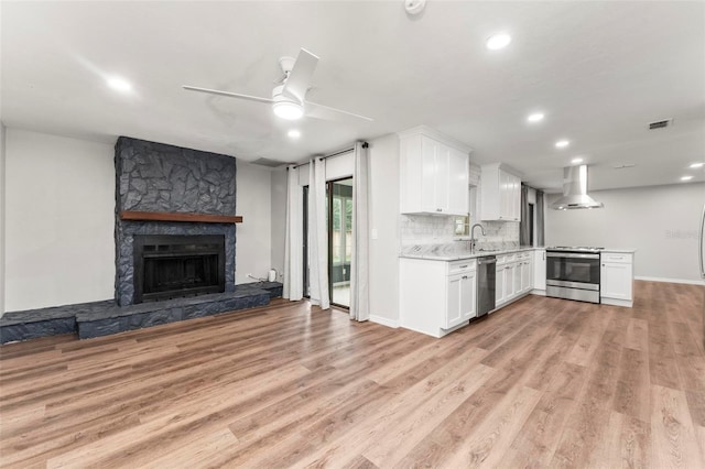 kitchen with white cabinets, light wood-type flooring, stainless steel appliances, wall chimney exhaust hood, and ceiling fan