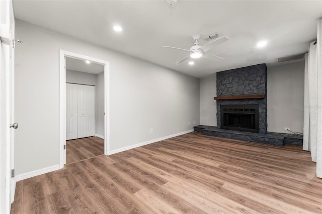 unfurnished living room featuring wood-type flooring, ceiling fan, and a stone fireplace