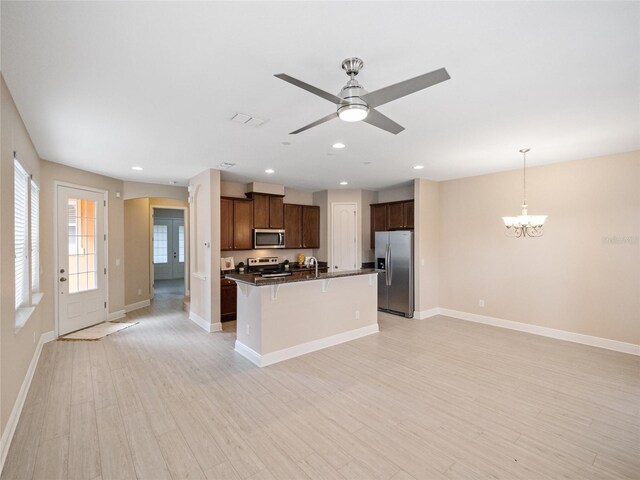 kitchen with pendant lighting, light wood-type flooring, stainless steel appliances, and an island with sink