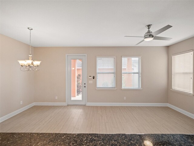 spare room featuring a healthy amount of sunlight, ceiling fan with notable chandelier, and wood-type flooring