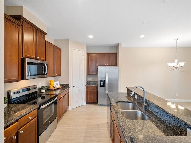 kitchen featuring sink, stainless steel appliances, an inviting chandelier, dark stone countertops, and decorative light fixtures