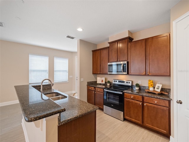 kitchen with sink, stainless steel appliances, light hardwood / wood-style floors, and an island with sink