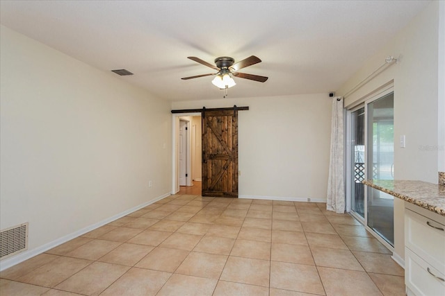 spare room featuring ceiling fan, light tile patterned flooring, and a barn door