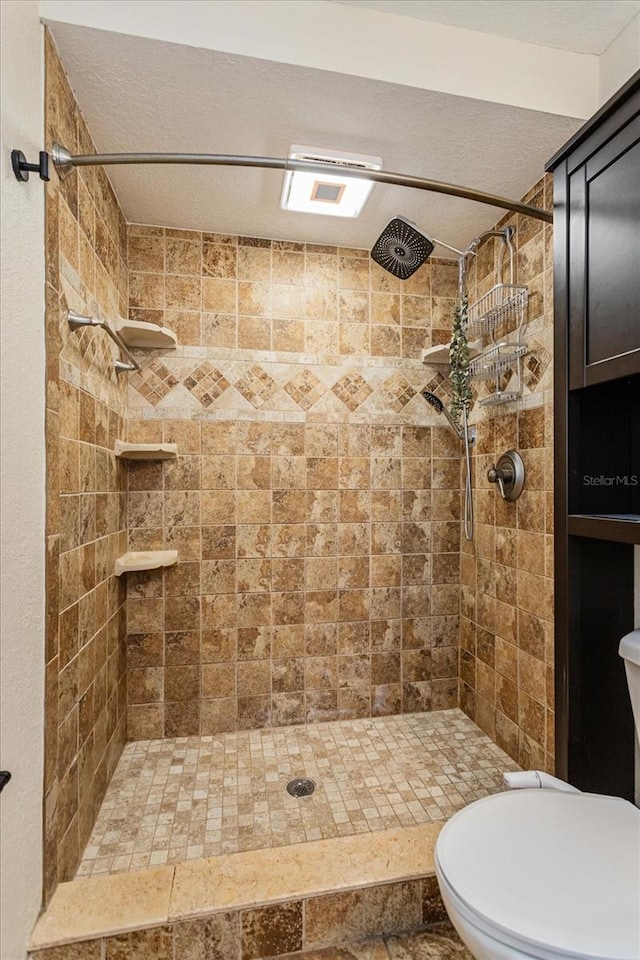 bathroom with a textured ceiling, tiled shower, and toilet