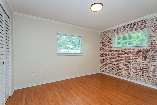 empty room featuring wood-type flooring, ornamental molding, and brick wall