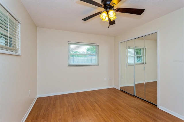 unfurnished bedroom with a textured ceiling, ceiling fan, a closet, and hardwood / wood-style flooring