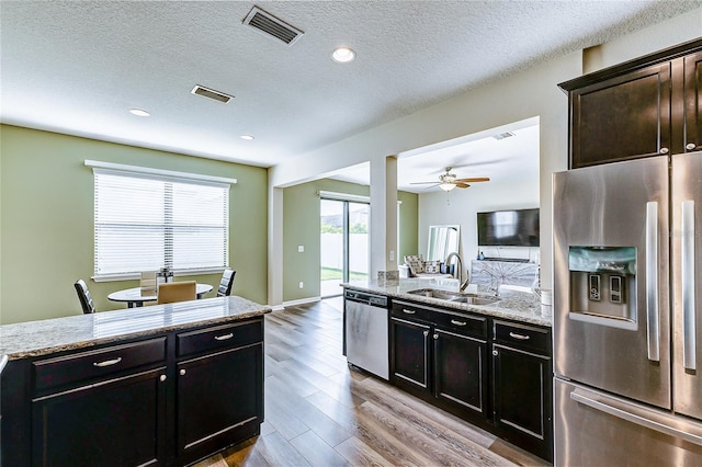 kitchen featuring ceiling fan, sink, stainless steel appliances, light stone countertops, and light hardwood / wood-style floors