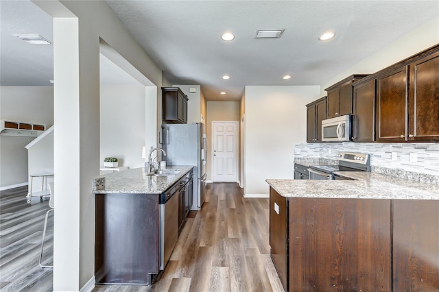 kitchen featuring kitchen peninsula, dark brown cabinets, appliances with stainless steel finishes, light wood-type flooring, and decorative backsplash