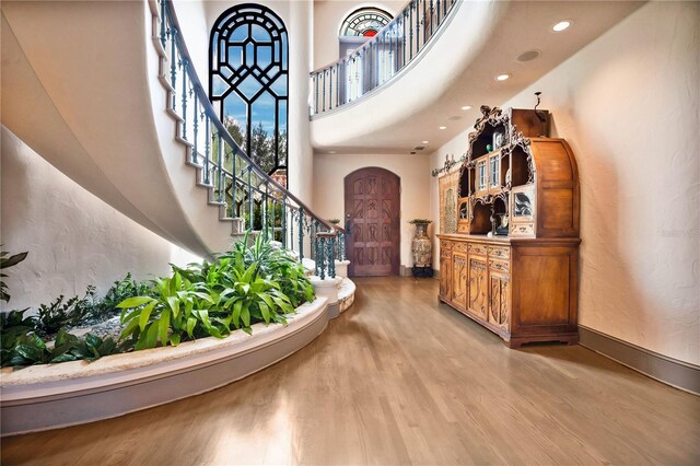 foyer featuring arched walkways, wood finished floors, a towering ceiling, baseboards, and stairs