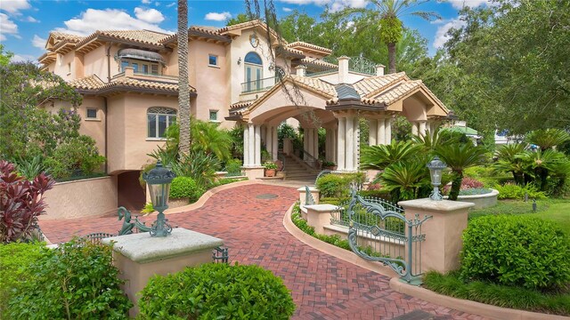 mediterranean / spanish-style home with a gate, a tile roof, and stucco siding