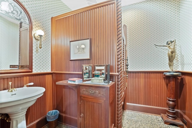 bathroom with a wainscoted wall, a sink, and wallpapered walls