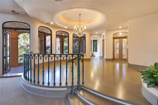 interior space featuring a tray ceiling, french doors, arched walkways, a chandelier, and baseboards