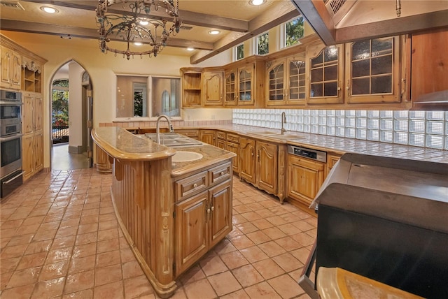 kitchen featuring arched walkways, a kitchen island with sink, a sink, open shelves, and beamed ceiling