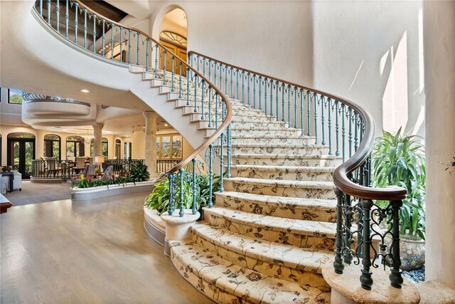 stairs featuring a high ceiling, wood finished floors, and ornate columns