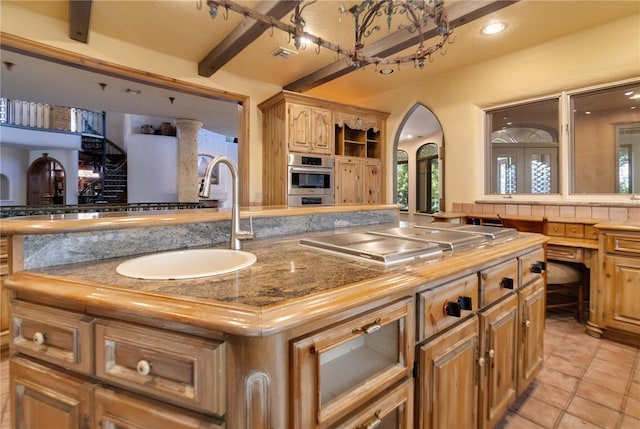 kitchen featuring cooktop, visible vents, a kitchen island, beamed ceiling, and a sink