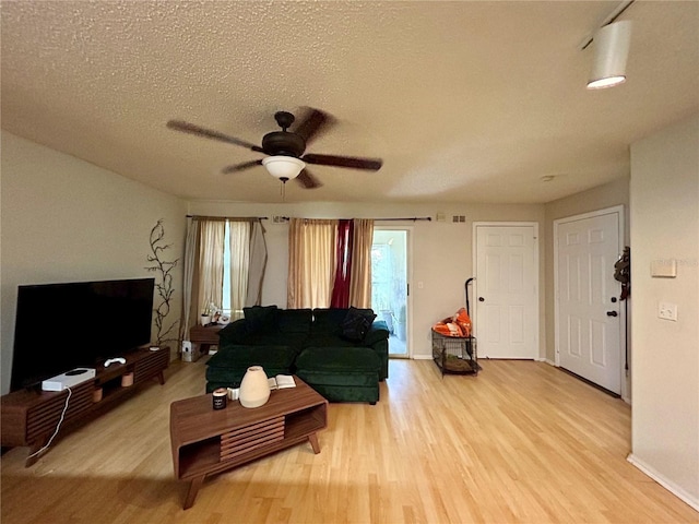 living room with a textured ceiling, ceiling fan, and light wood-type flooring