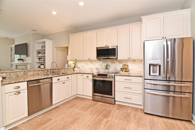 kitchen featuring white cabinets, light stone countertops, stainless steel appliances, and sink