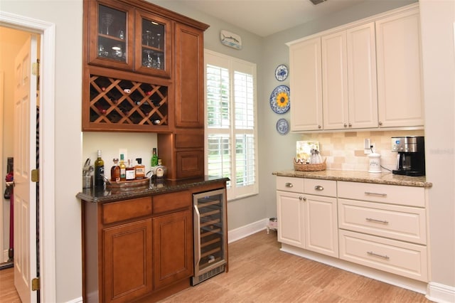 bar with stone countertops, a wealth of natural light, light hardwood / wood-style flooring, and wine cooler