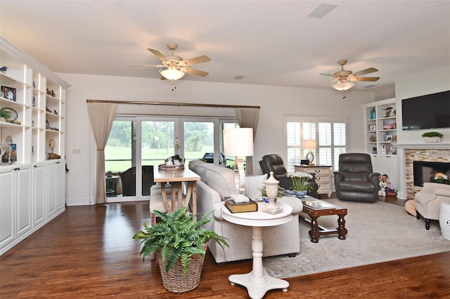 living room featuring a wealth of natural light, dark hardwood / wood-style flooring, and a stone fireplace