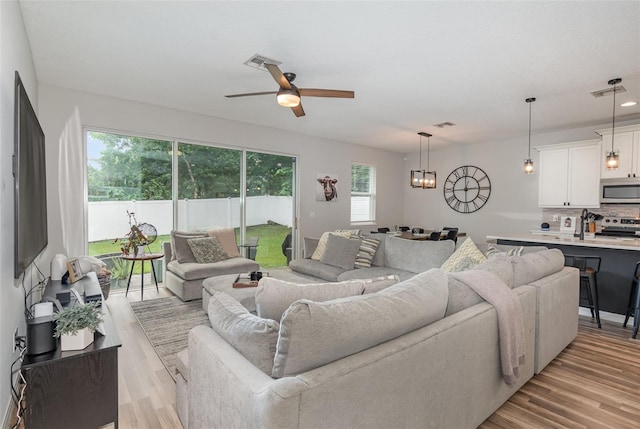 living room featuring a healthy amount of sunlight, ceiling fan with notable chandelier, and light hardwood / wood-style flooring