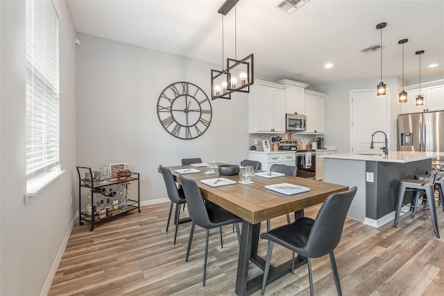 dining area with light wood-type flooring, an inviting chandelier, and sink