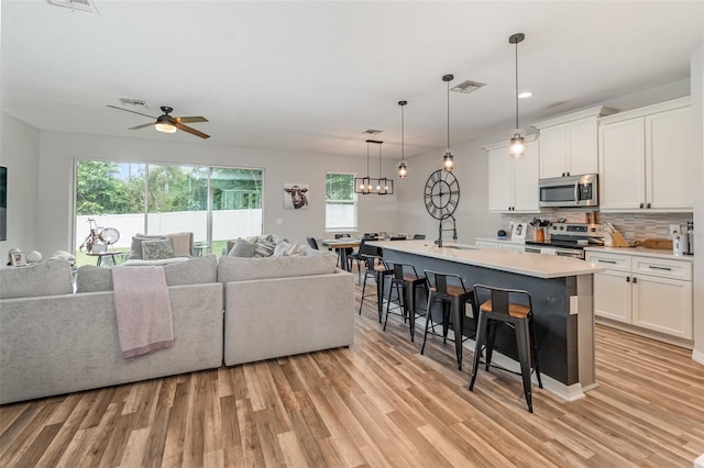 interior space featuring an island with sink, ceiling fan, appliances with stainless steel finishes, and white cabinetry