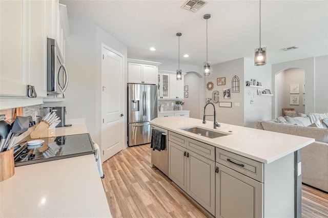 kitchen featuring hanging light fixtures, appliances with stainless steel finishes, white cabinetry, sink, and a kitchen island with sink